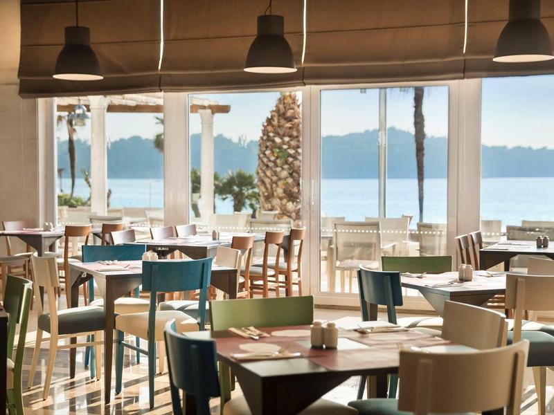 Brightly furnished restaurant with wooden furniture and view of water and beach.