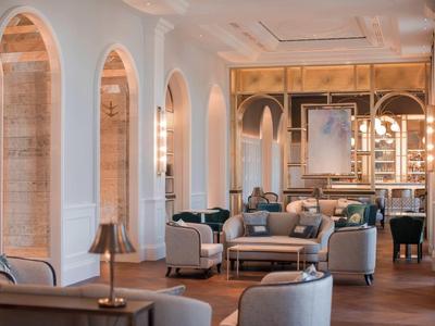 Elegante area lounge dell'hotel con pareti bianche, finestre ad arco e comodi arredi.