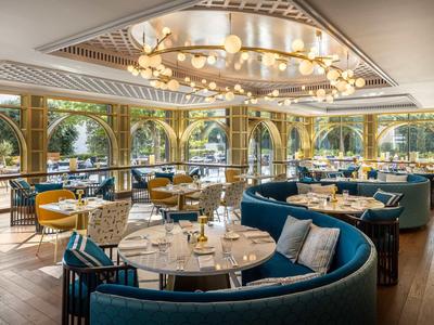 Ristorante elegante con divani blu, tavoli rotondi e grandi finestre con vista.