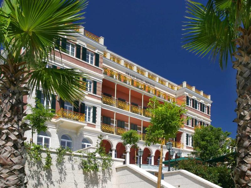 Edificio di un hotel su più piani con balconi, palme e cielo azzurro limpido.