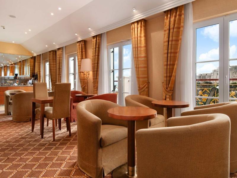 Area lounge elegante dell'hotel con comode poltrone, tavoli e ampie finestre con vista esterna.