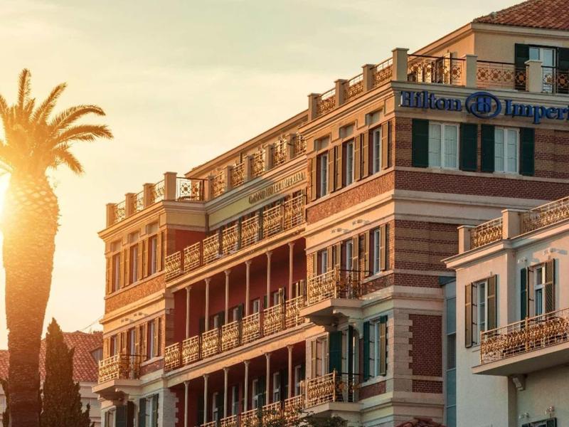 Edificio dell'hotel con balconi al tramonto accanto a una palma.