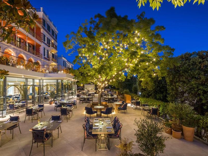 Terrazza dell'hotel di sera con albero illuminato e tavoli apparecchiati sotto un cielo terso.