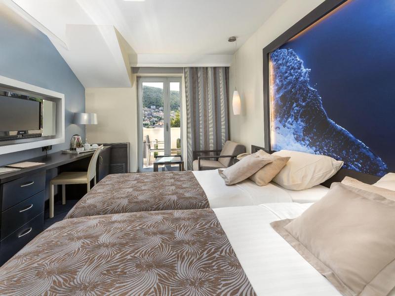 Camera d'hotel moderna con letto grande, TV a parete e accesso a un balcone luminoso.