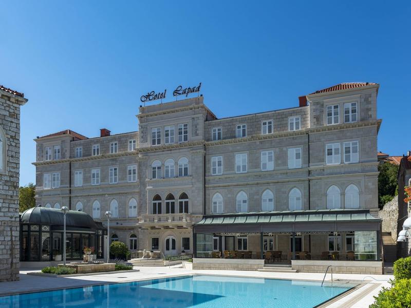 Grande hotel storico con piscina sotto un cielo azzurro limpido.