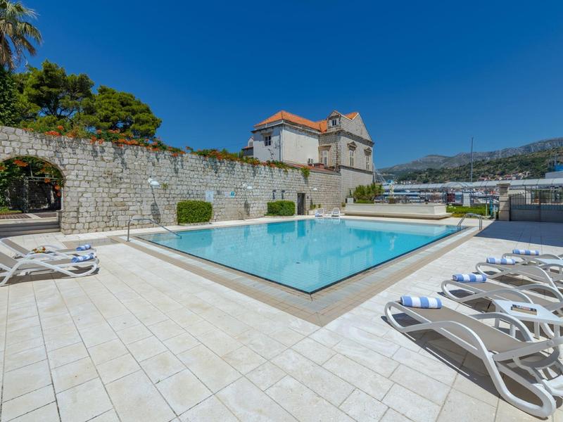 Una piscina all'aperto limpida con lettini e muro di pietra antica sotto un cielo soleggiato.