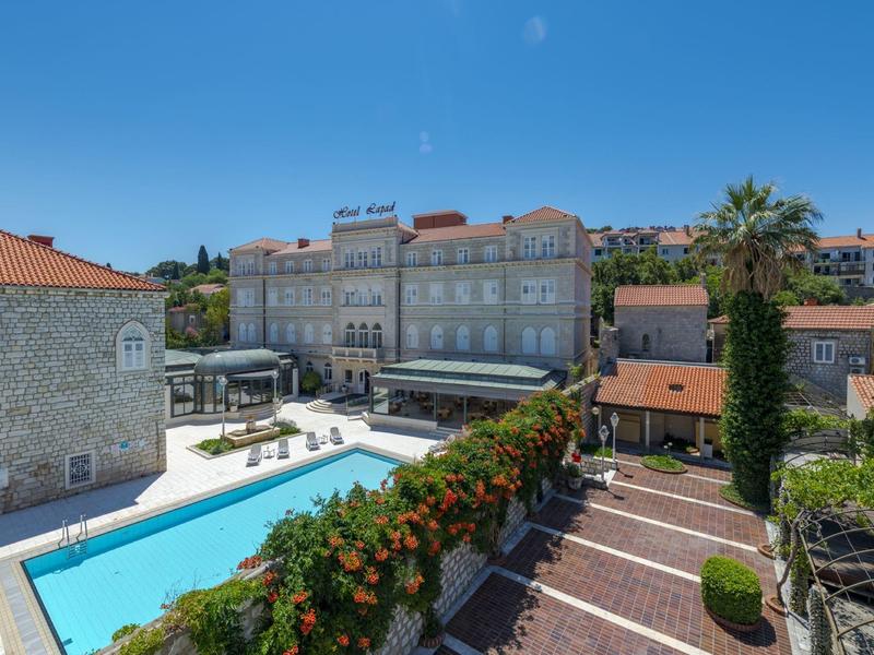 Hotel con piscina all'aperto, terrazza soleggiata e vegetazione mediterranea sotto un cielo limpido.