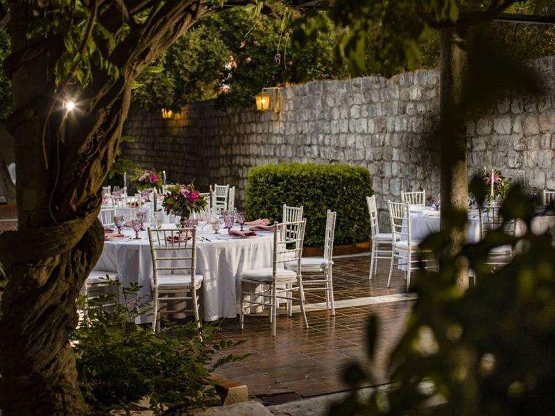 Festa serale in giardino con tavoli apparecchiati e sedie bianche sotto gli alberi illuminati.