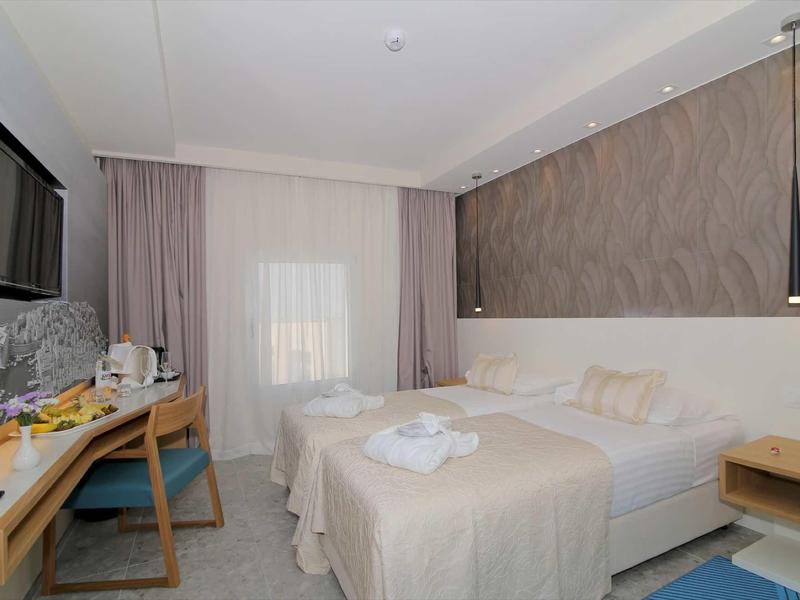 Camera d'hotel luminosa con letto matrimoniale, scrivania, sedia e TV a muro.