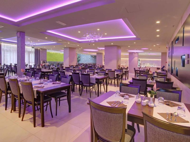Ristorante moderno con illuminazione viola, tavoli e sedie disposti.