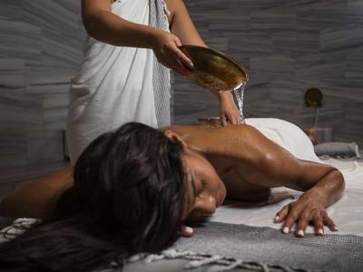 Donna che riceve un massaggio a spalle e schiena in una spa moderna con pareti scure.