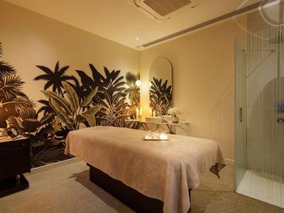 Accogliente stanza benessere con lettino da massaggio e decorazione murale tropicale.