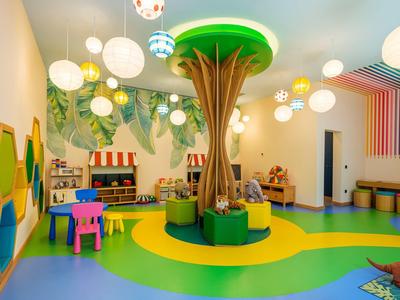 Sala giochi colorata per bambini con grande scultura ad albero al centro e lampade luminose.