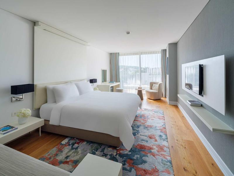 Camera d'hotel moderna con letto grande, pavimento in legno e vista sulla città da grandi finestre.