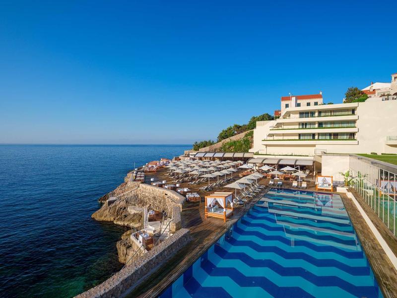 Hotel con piscina all'aperto e terrazza solarium su una scogliera sopra il mare.