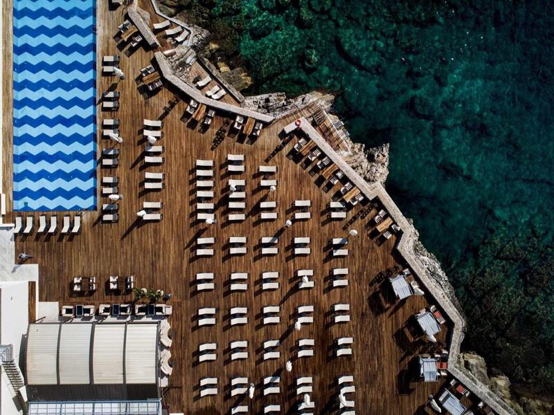 Vista aerea di una piscina dell'hotel con lettini e costa rocciosa vicino al mare.