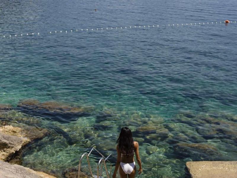 Donna con cappello su scala di pietra vicino all'acqua limpida con isola e collina boschiva sullo sfondo.
