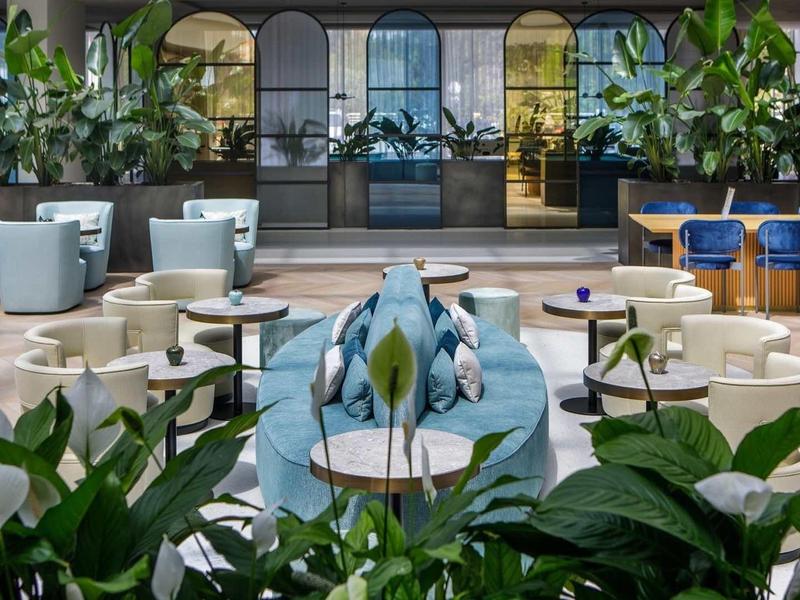 Area lounge moderna dell'hotel con divani blu, sedie e piante verdi.