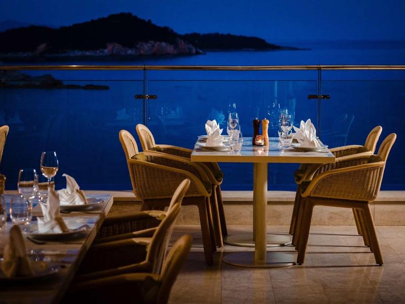 Ristorante con terrazza elegante di sera con vista su acque tranquille e montagne.
