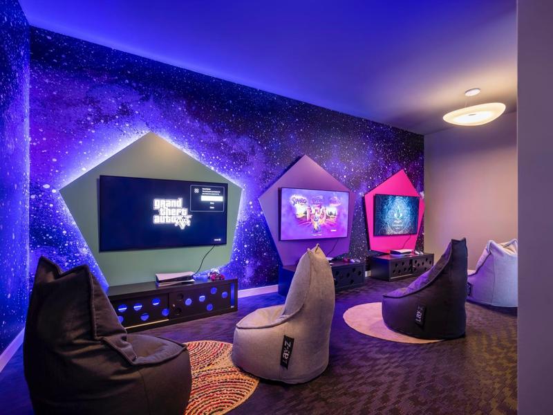 Area giochi moderna con pouf e murale cosmico in un hotel.