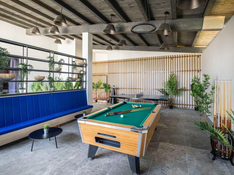 Sala moderna con tavolo da biliardo, panchine blu e piante in un hotel.