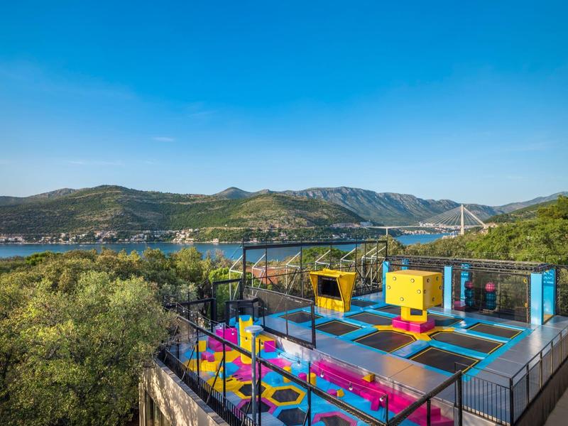 Skywalk colorato con funivie davanti a colline boschive e cielo azzurro.