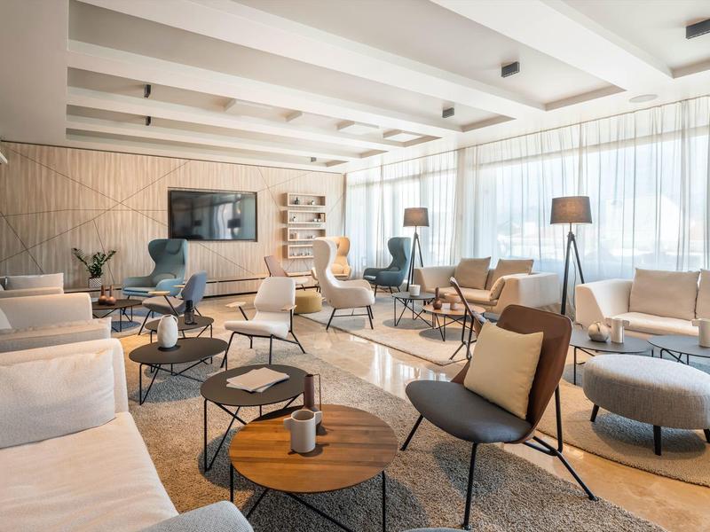 Sala d'hotel luminosa e moderna con poltrone comode e ampie finestre.