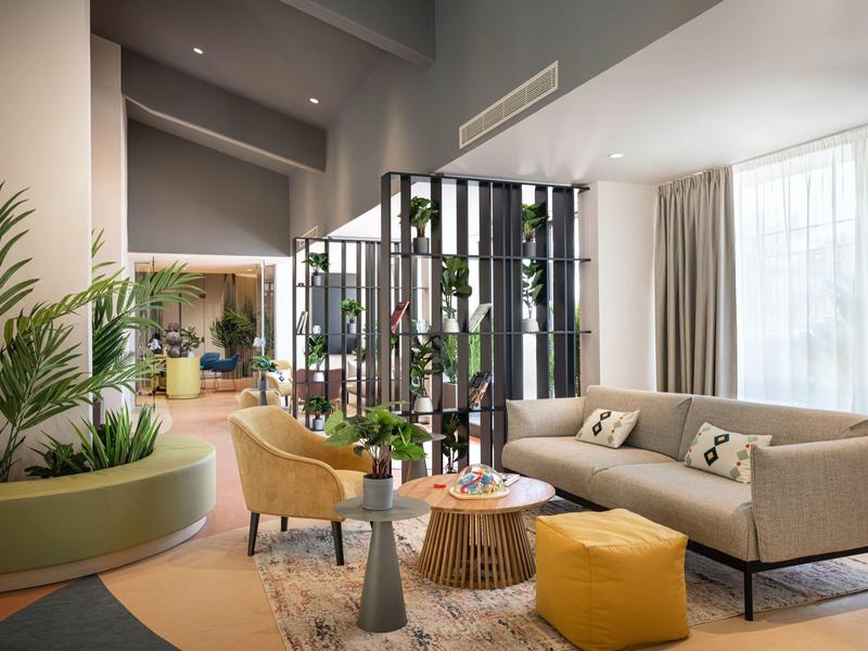 Area lounge luminosa e moderna con divano, poltrone, piante e divisori in un hotel.