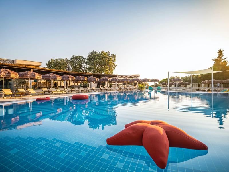 Grande piscina dell'hotel con giocattolo a forma di stella marina rossa e tramonto sullo sfondo.