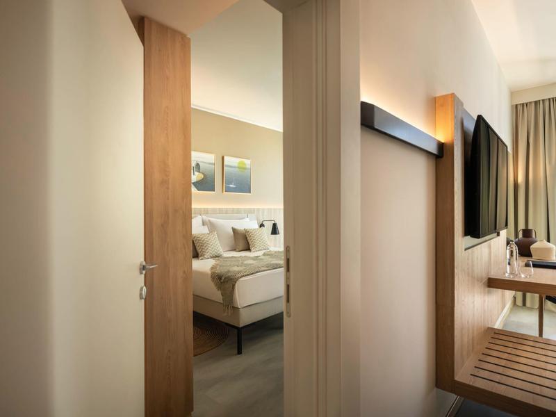 Vista attraverso porta aperta su una stanza d'hotel elegante con letto e decorazioni murali.