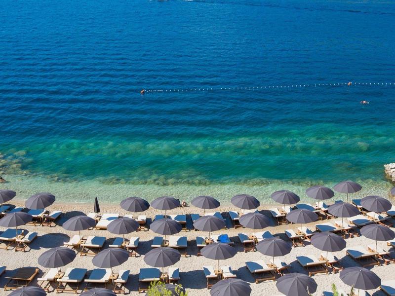 Spiaggia con file di ombrelloni accanto all'acqua blu trasparente.