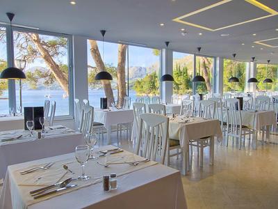 Brightly furnished restaurant with white tables and sea view through large windows.