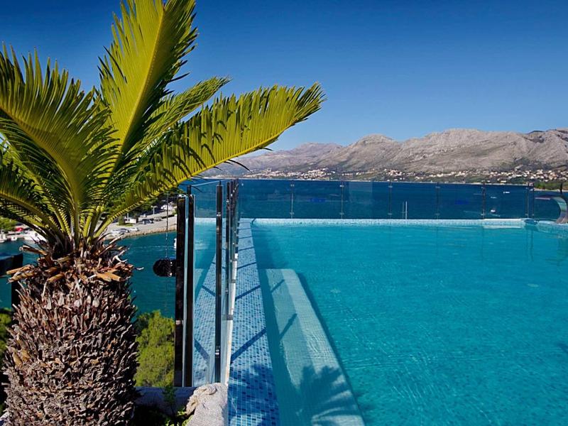 Piscina a sfioro dell'hotel con vista sul mare e sulle montagne sotto un cielo sereno.