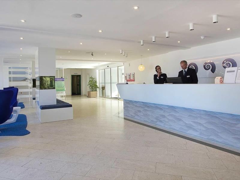 Hall dell'hotel luminosa con banco reception moderno e due dipendenti.