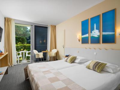 Camera d'albergo luminosa con due letti e balcone con vista sul giardino.