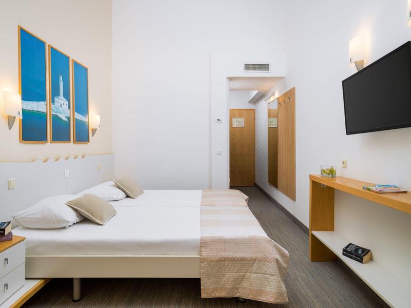 Camera d'hotel luminosa con letto matrimoniale, quadro a parete, TV e arredi moderni.