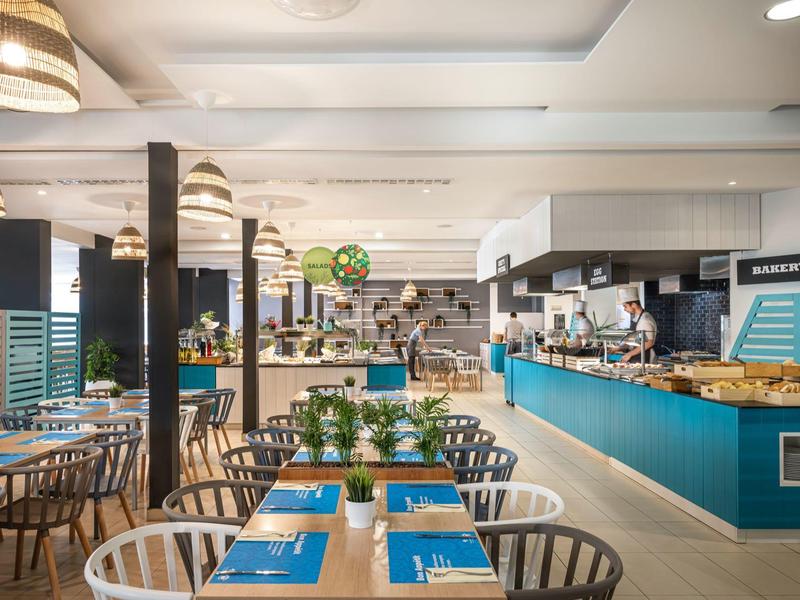 Ristorante moderno con tavoli blu, sedie bianche e un banco di servizio aperto.