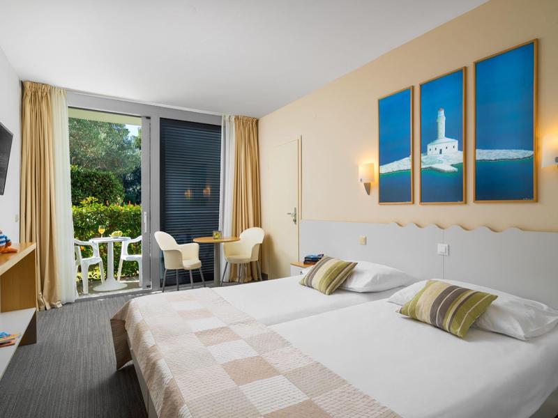 Camera d'albergo luminosa con due letti e balcone con vista sul giardino.