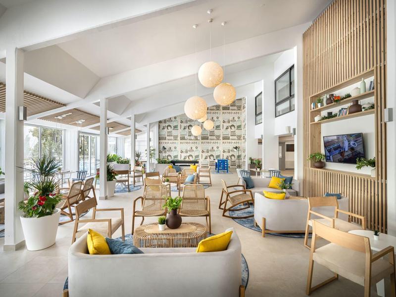 Hall di un hotel moderno e luminoso con aree salotto accoglienti e piante decorative.