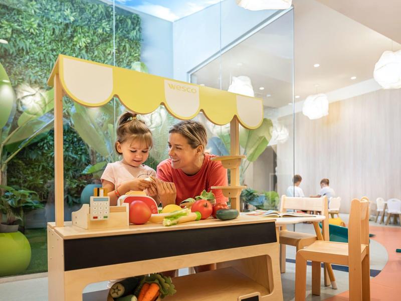 Bambina e assistente che giocano a un tavolo colorato in una stanza luminosa.