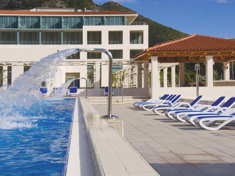 Lettini a bordo piscina accanto a una cascata in un hotel moderno con vista sulle montagne.