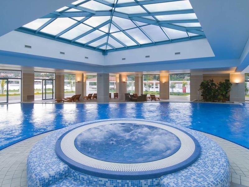 Piscina interna con soffitto a lucernario e vasca idromassaggio circolare in primo piano in spa dell'hotel.