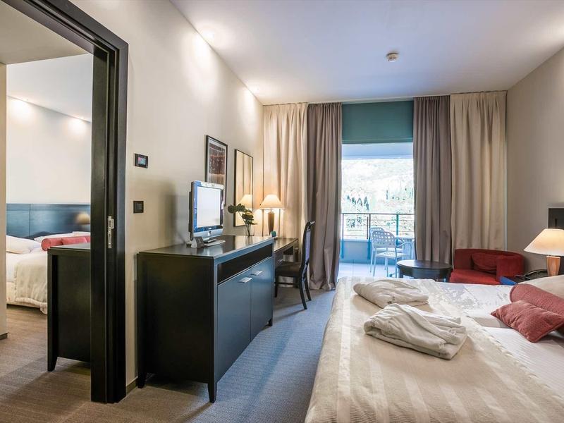 Camera d'hotel moderna con letto, scrivania, TV e balcone con vista sulla città.