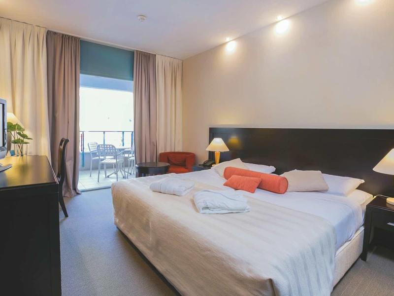 Camera d'hotel con letto matrimoniale, lampade da comodino, TV e balcone con posti a sedere esterni.