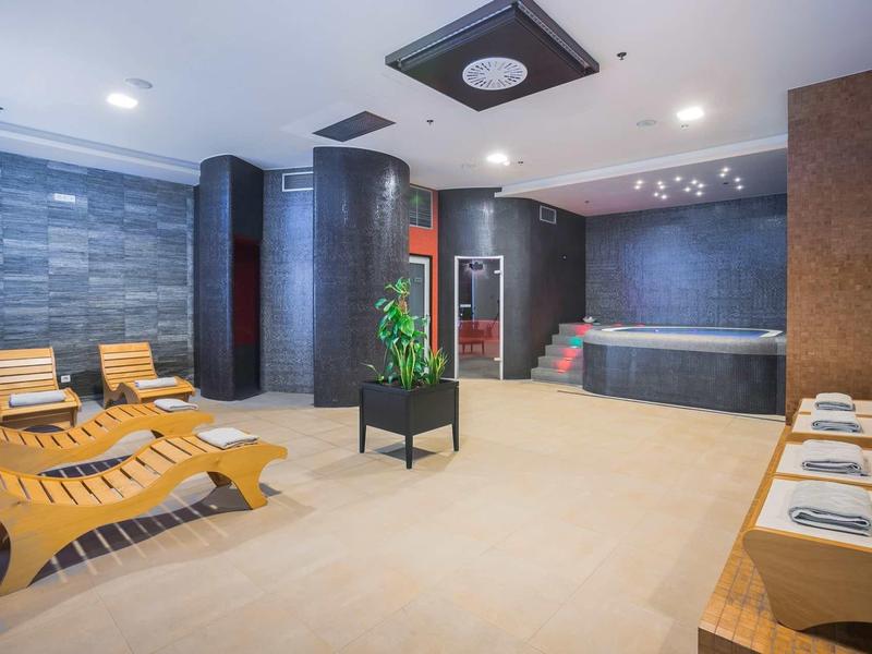 Area spa moderna con lettini in legno, pareti in pietra e vasca idromassaggio.