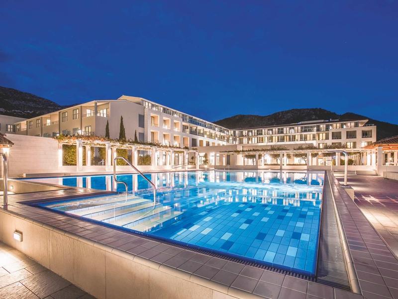 Hotel di lusso di notte con grande piscina illuminata e montagna sullo sfondo.