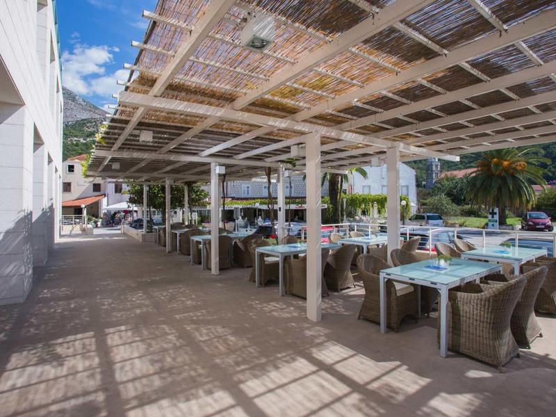 Area pranzo all'aperto con tavoli e sedie sotto una pergola ombreggiata in una giornata di sole.