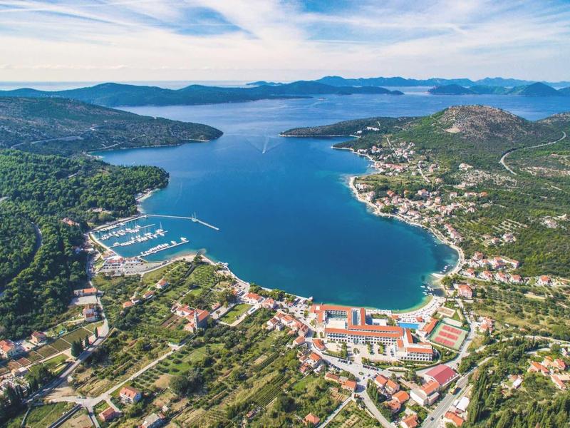 Una baia costiera con acqua azzurra limpida circondata da colline verdi e piccoli paesi lungo la costa.
