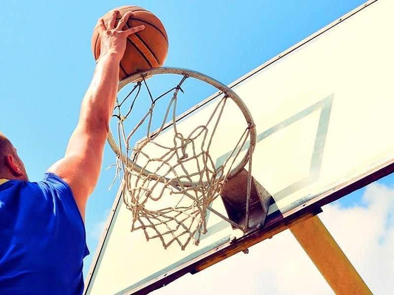 Persona in blu che lancia una palla da basket verso il canestro sotto un cielo sereno.