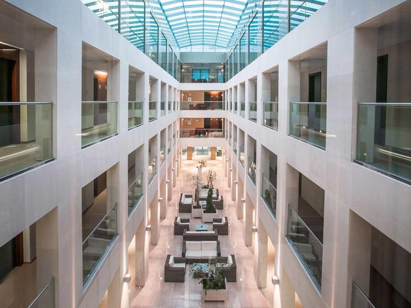 Luminoso atrio dell'hotel con pareti bianche, soffitto in vetro e mobili moderni al centro.